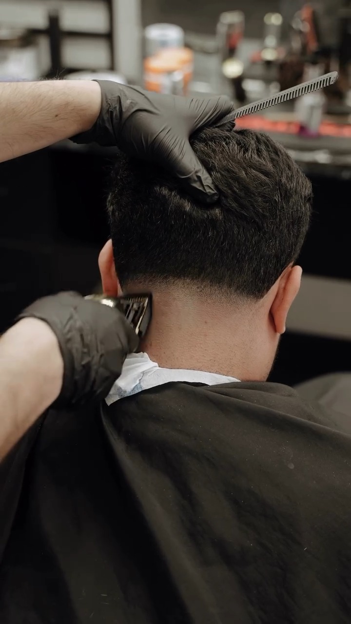 Barber met handschoenen werkt met de tondeuse in de nek van een klant