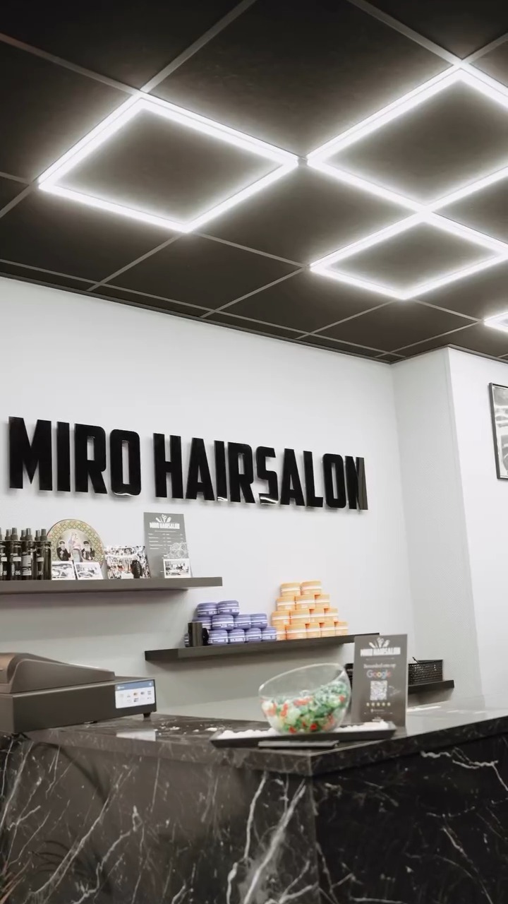 De zaak van binnen: lichtpanelen aan het plafond, de witte muur met MIRO HAIRSALON in zwarte letters en de zwarte marmeren toonbank